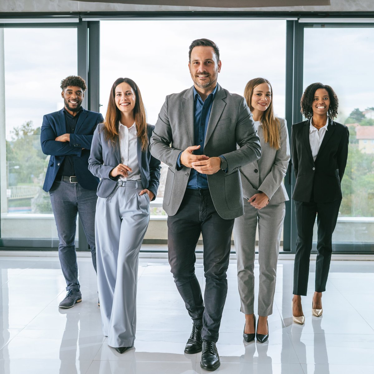 Diverse group of confident business professionals walking toward camera in a bright modern office, smiling and united in teamwork, leadership and a positive, determined future